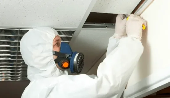 Asbestos abatement technician in full PPE inspecting ceiling
